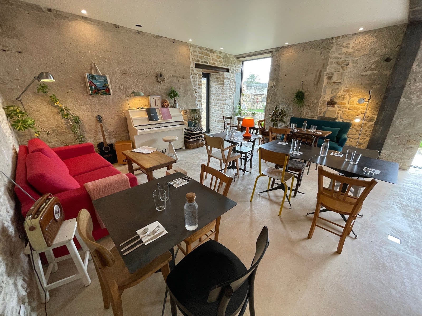 Bright coworking space with large wooden desks, chairs, warm light, and rustic walls with large windows overlooking the courtyard.