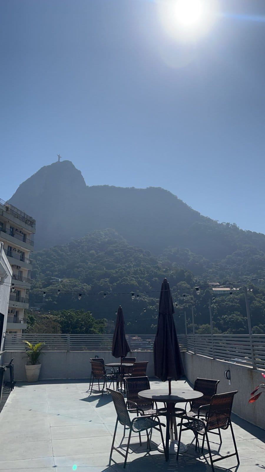Rooftop terrace with tables and umbrellas overlooking Christ the Redeemer at Vivére Coliving in Rio de Janeiro