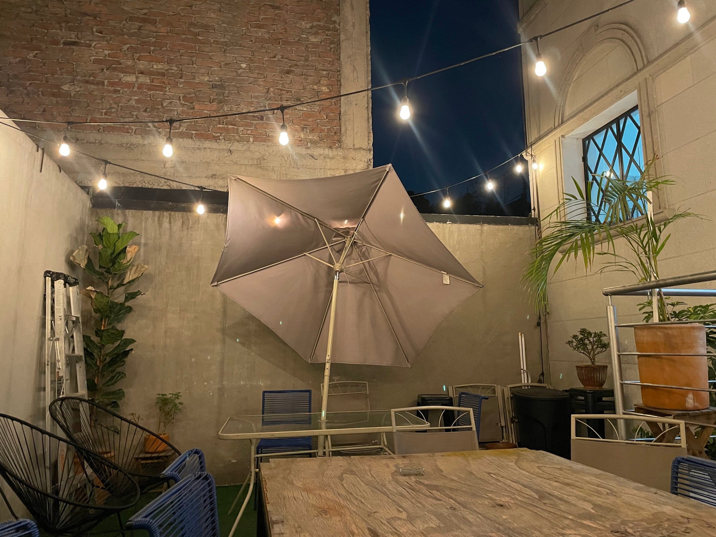 The U-Co Roma outdoor courtyard terrace at night with warm string lights, exposed brick walls and umbrella