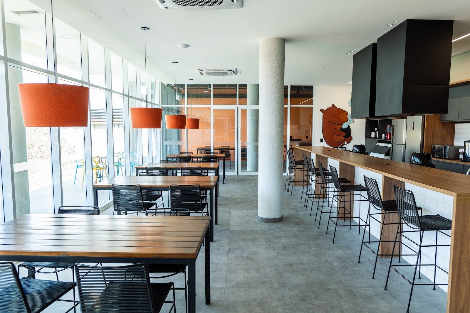 Bright communal dining and bar area with floor-to-ceiling windows at Uliving Campinas