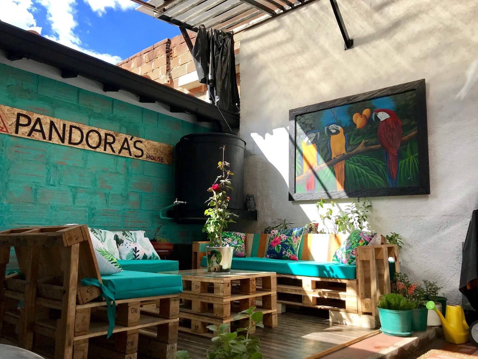Sunny outdoor terrace at Pandora's House Coliving with pallet seating, blue sky and the Pandora's House mural