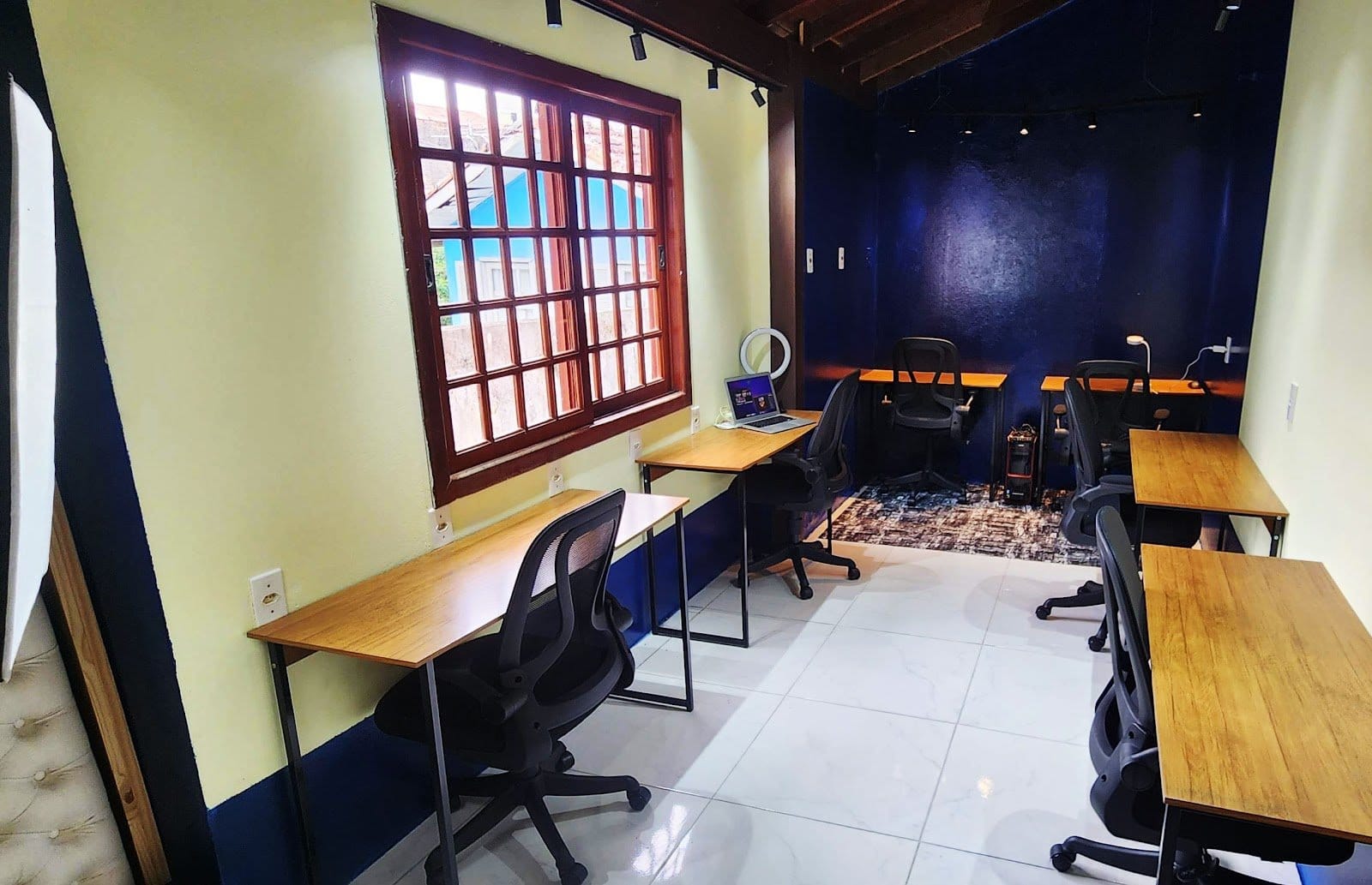 Dedicated coworking room with multiple desks, ergonomic chairs and a laptop in use at Casa Maré coliving in Florianópolis