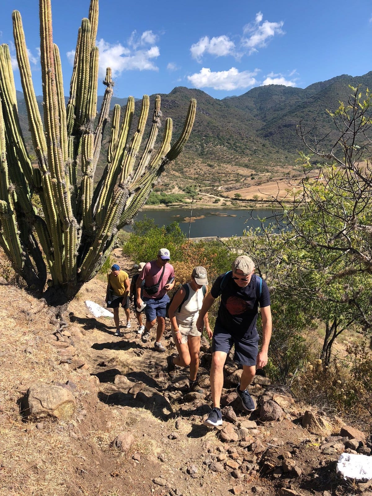 Group of Co404 Oaxaca residents hiking a cactus-lined trail with mountain lake views in the Oaxacan valley