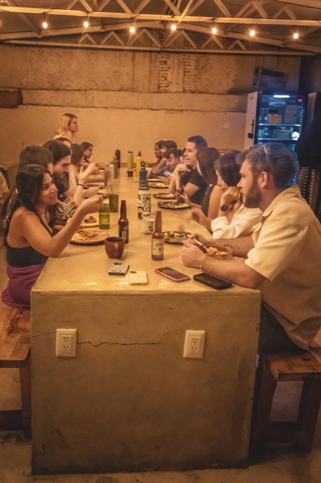 Large group of Co404 Oaxaca residents sharing a community dinner at the long concrete table under string lights