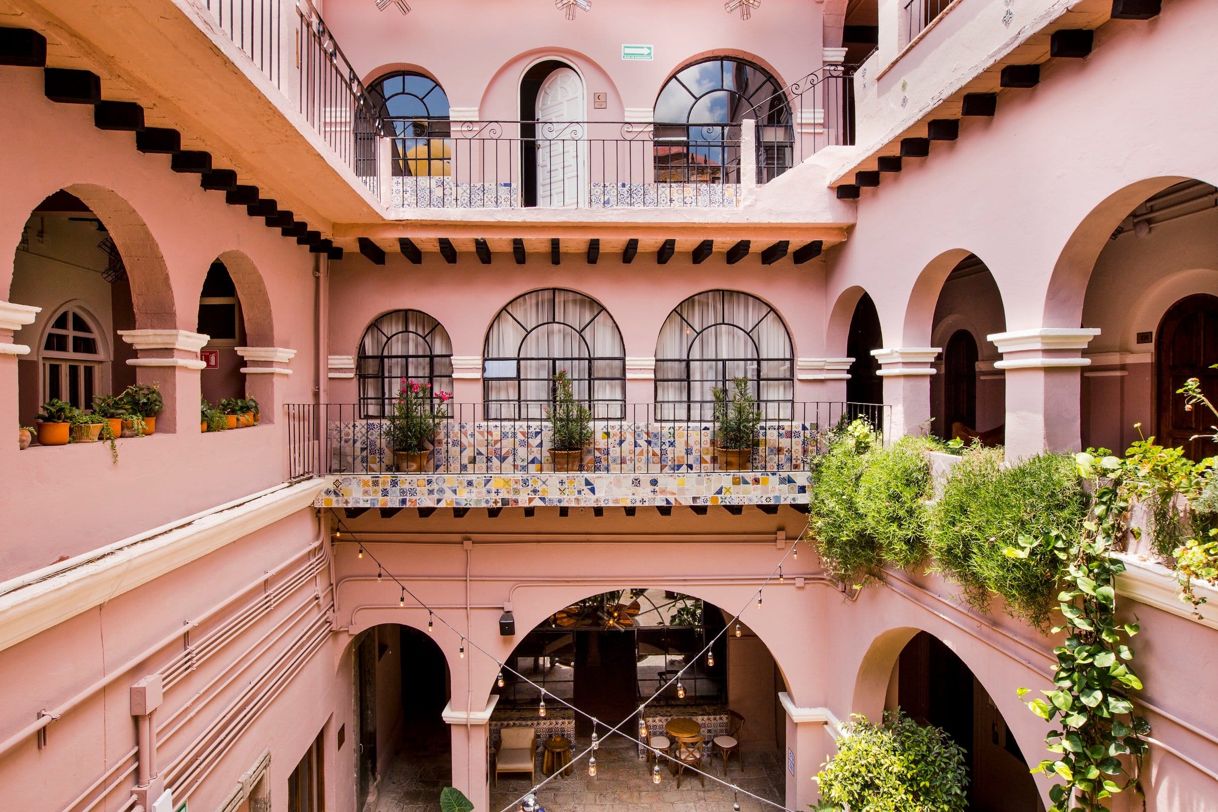 Two-story colonial atrium at Selina San Miguel de Allende with arched balconies, blue and white tile railings, and lush hanging plants
