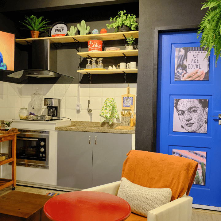 Eclectic shared kitchen with open shelving, plants and a bright blue Frida Kahlo door at Coliving Muní
