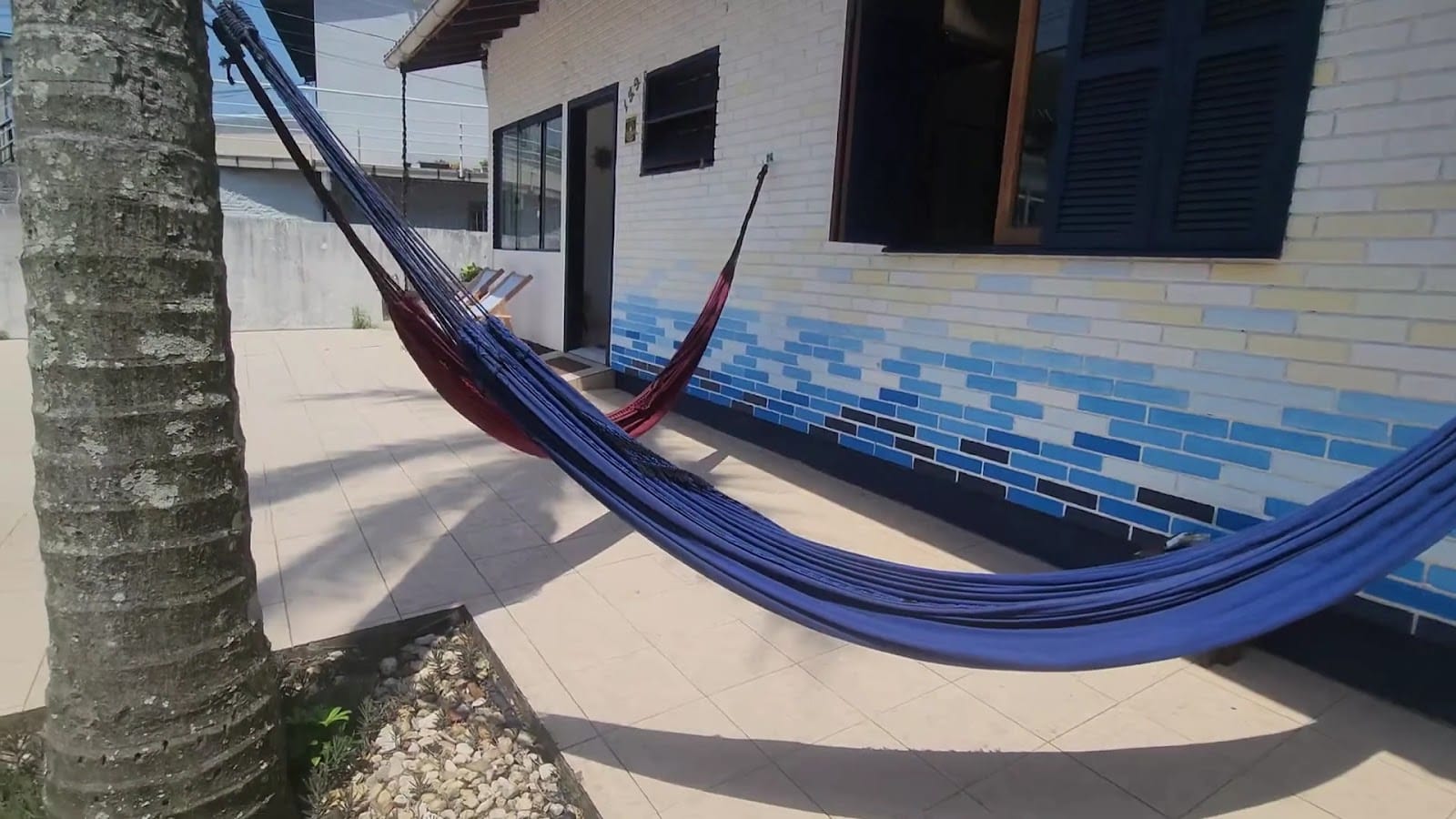 Hammocks strung across the tiled patio beside the blue-painted house at Casa Maré coliving in Florianópolis