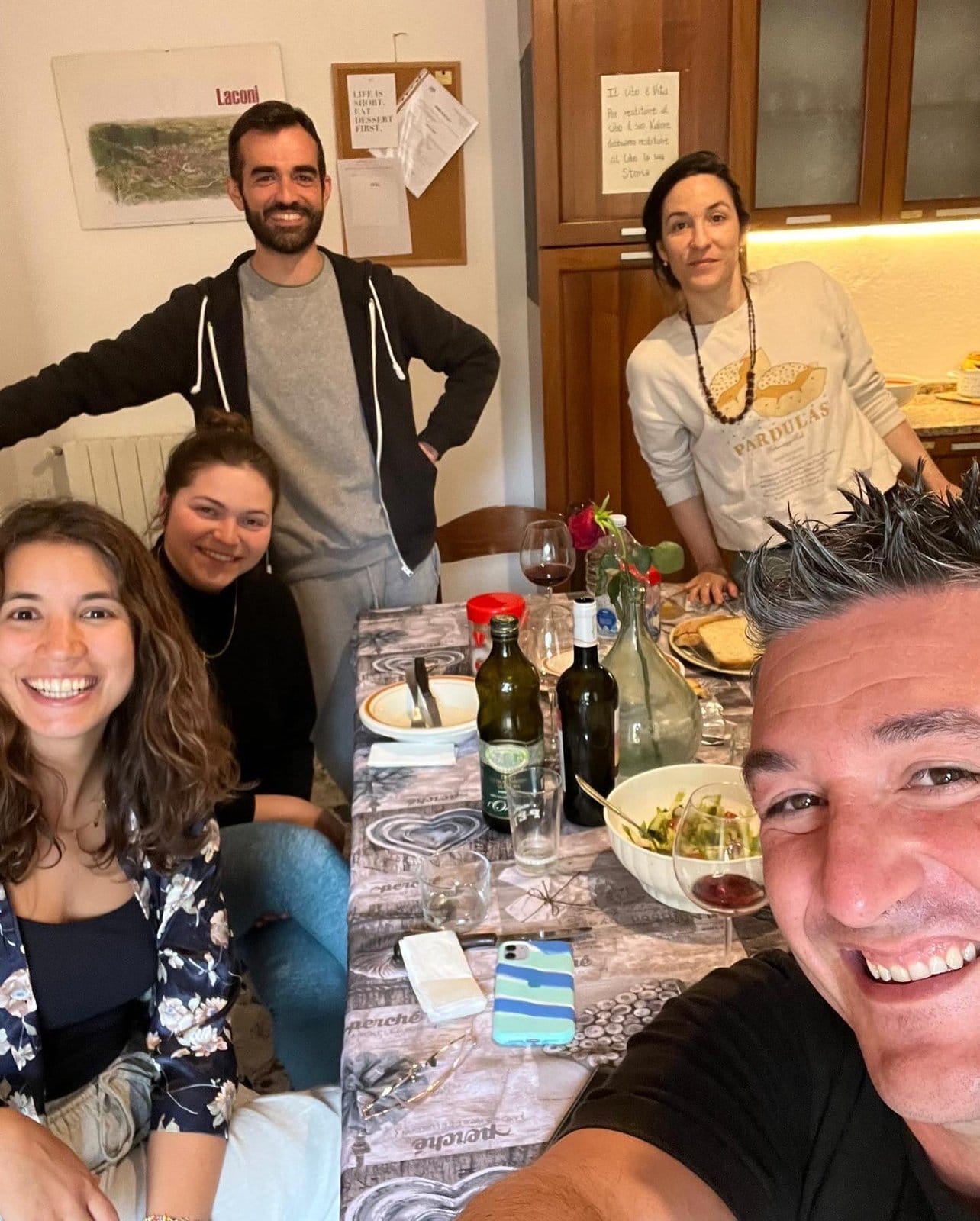 Hosts Carlo and Annalisa with guests sharing a casual meal with wine around the table inside Treballu Rural Coliving in the village of Laconi, Sardinia