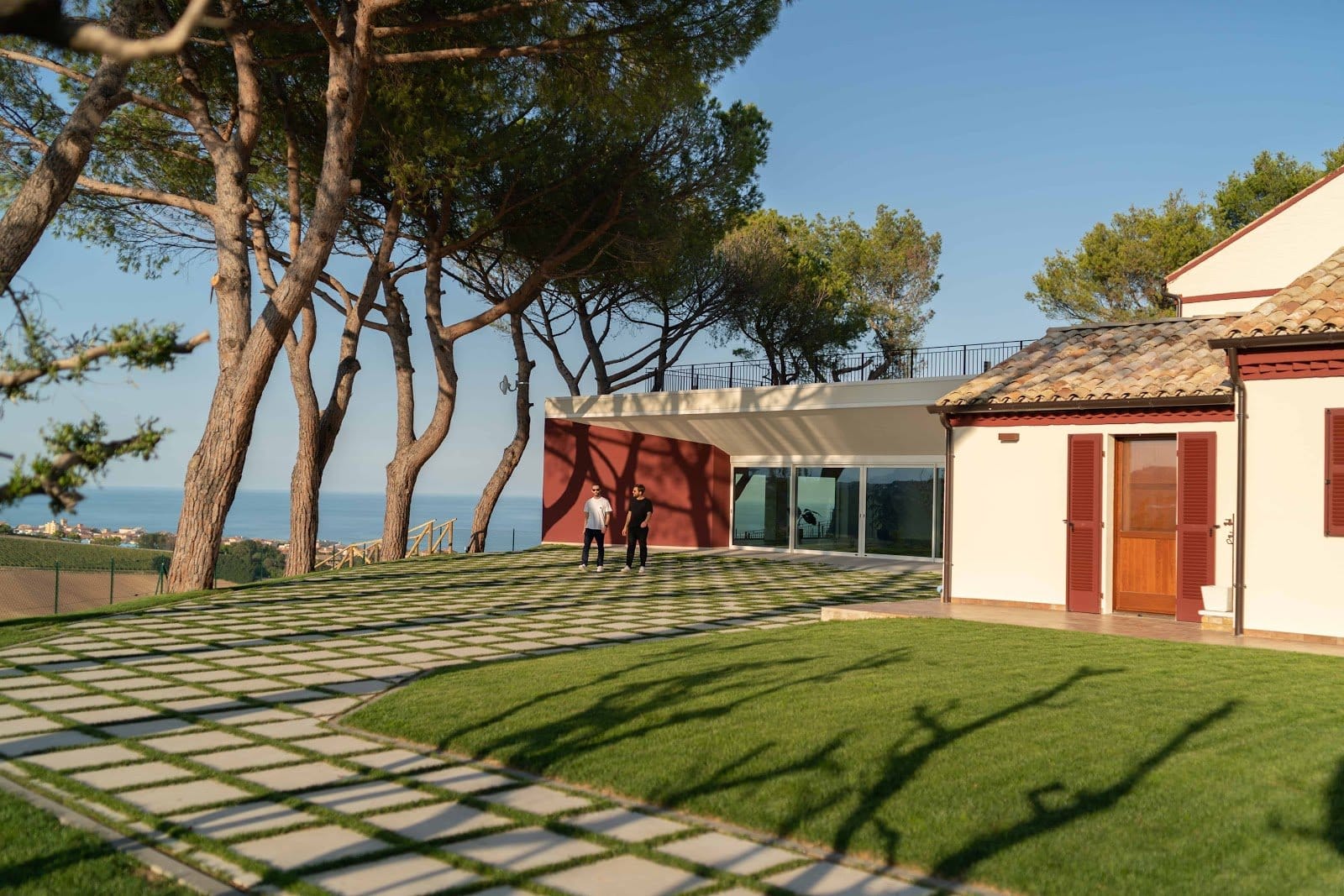 Daytime photo of two people walking and chatting on property lawn near building with tiled roof.