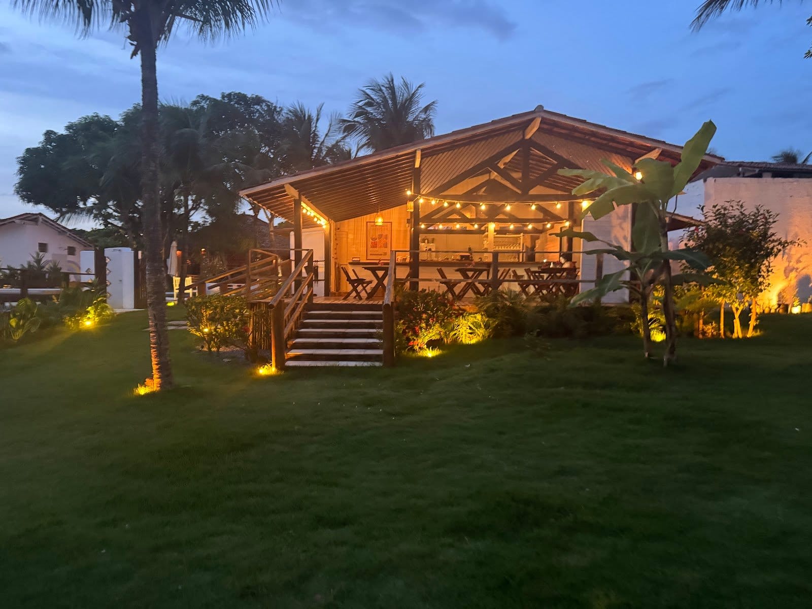 Thatched-roof open-air dining and bar pavilion lit with string lights at dusk at FlowHouse Jeri