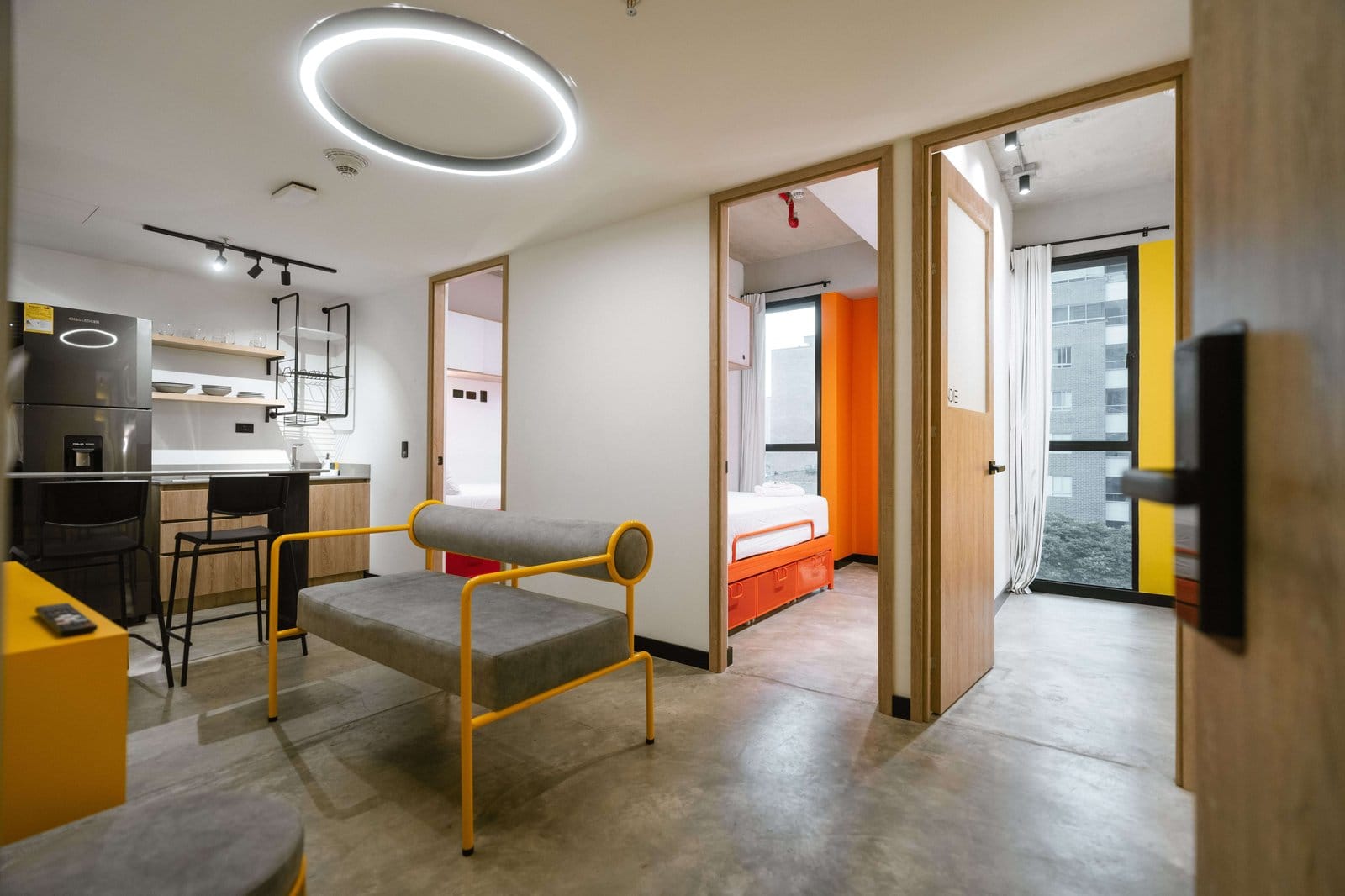 Shared apartment living area at Indie Studio with a yellow accent chair, open kitchen and adjoining bedrooms in Medellín