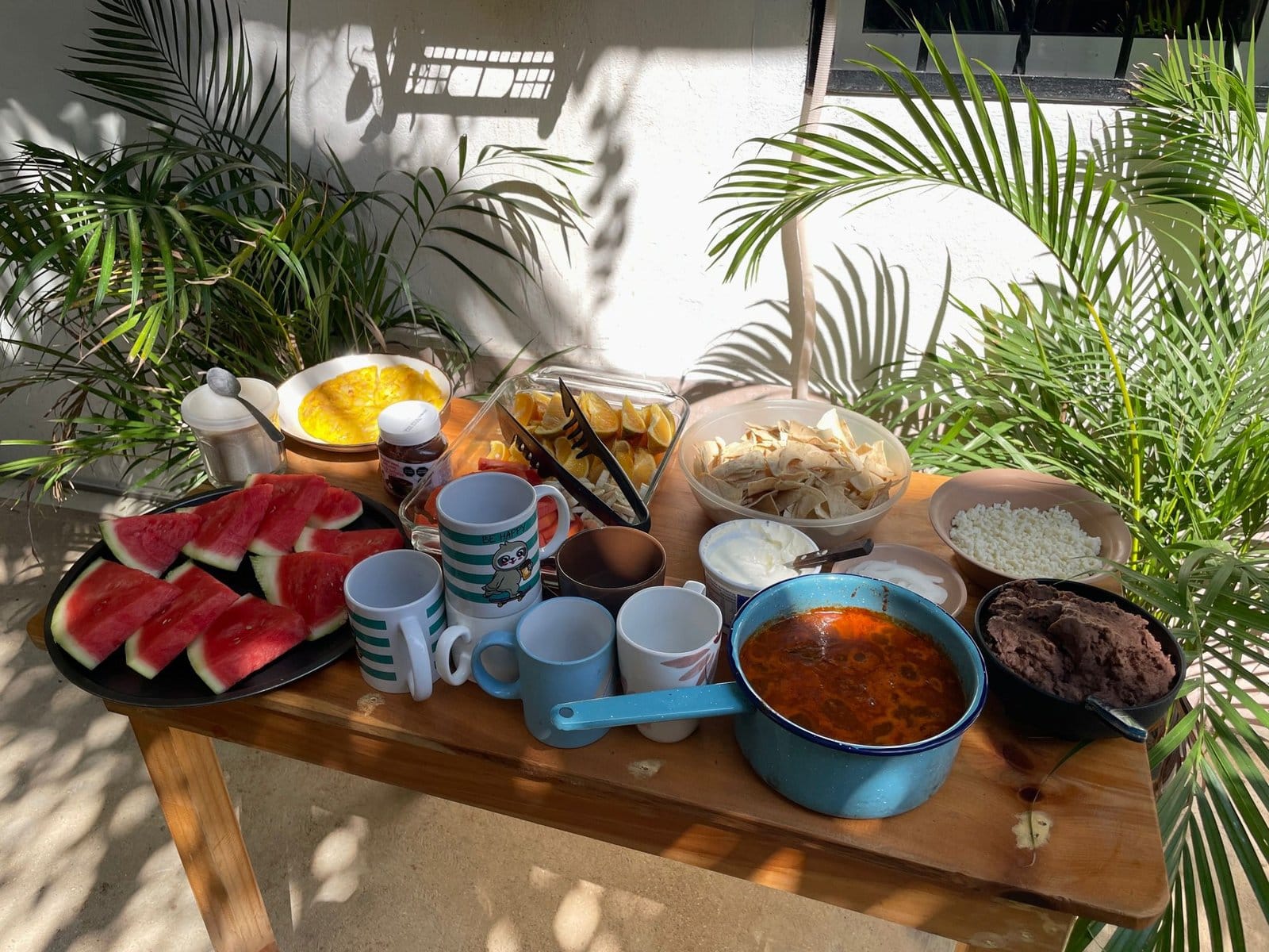 Community breakfast spread with watermelon, tortillas, beans and hot drinks on the outdoor communal table at Anana Coliving