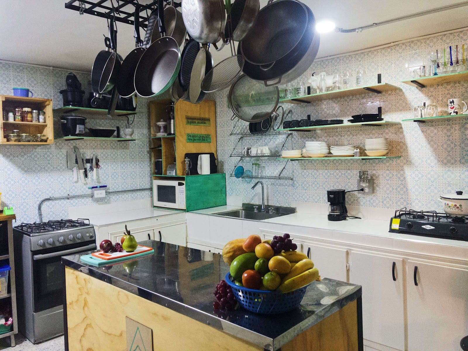 Bright communal kitchen at Pandora's House Coliving with hanging copper pots, tiled walls and a fresh fruit basket