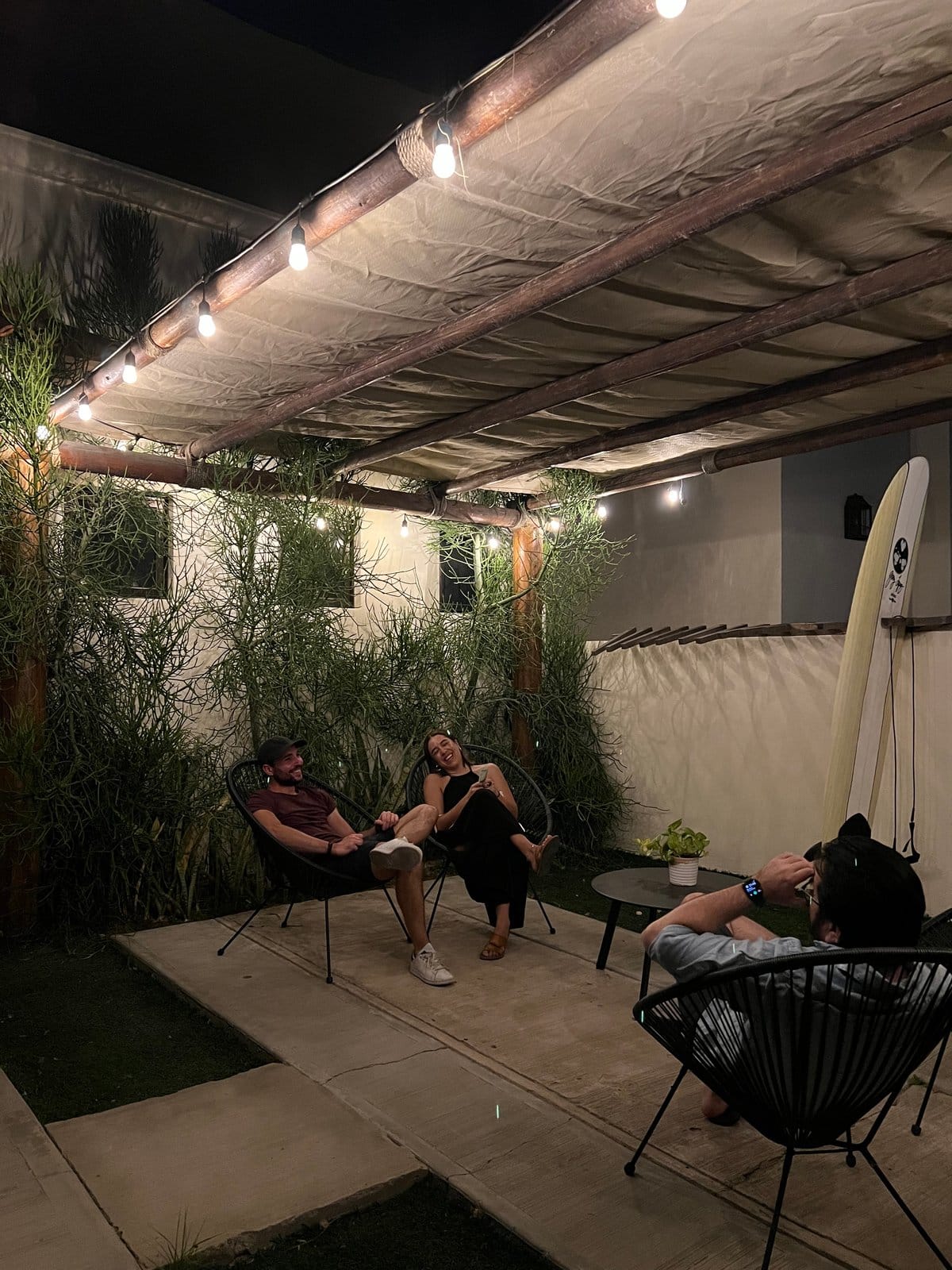 Three residents relaxing and chatting on the Outsite Los Cabos terrace at night with string lights