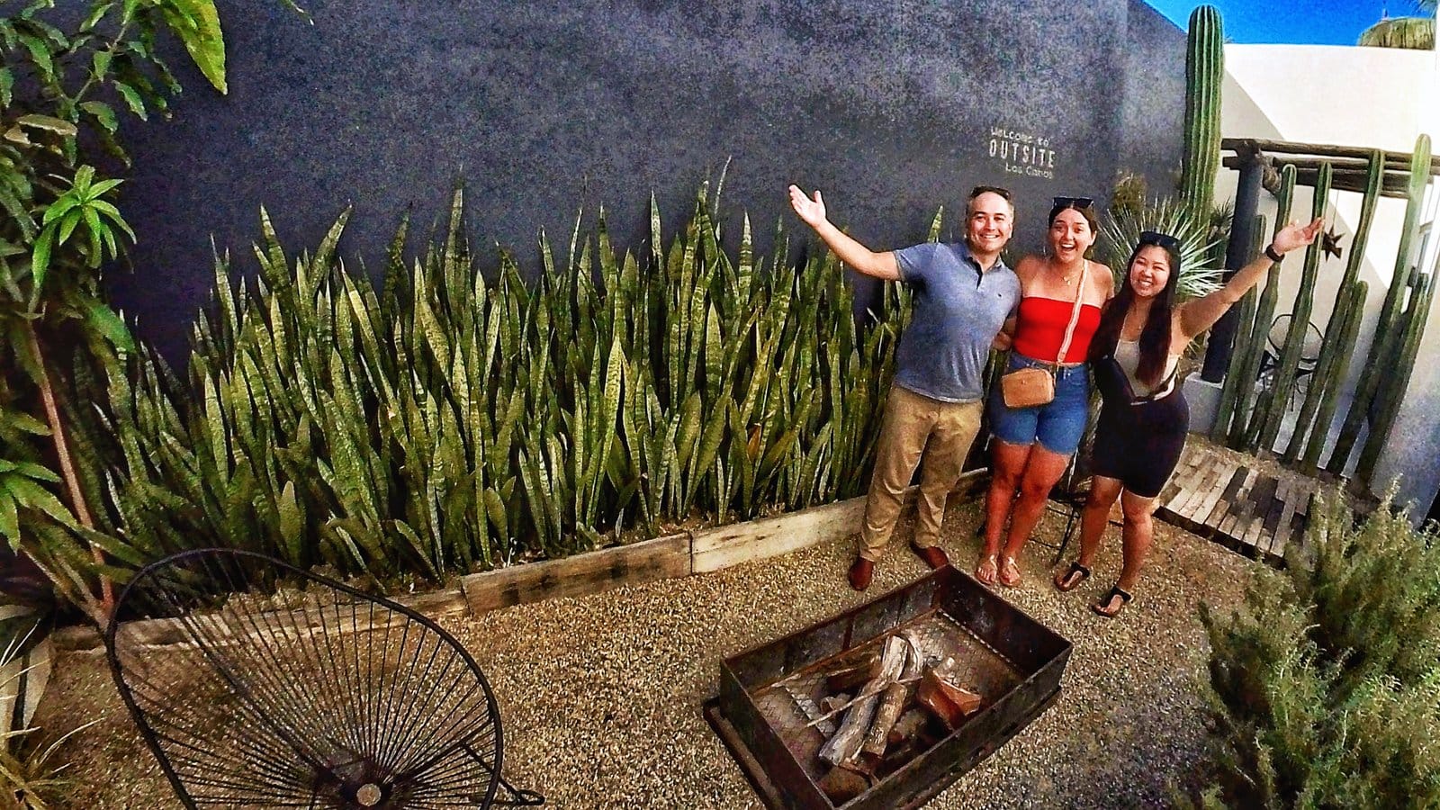 Three Outsite Los Cabos guests celebrating in the cactus garden with fire pit and dark feature wall