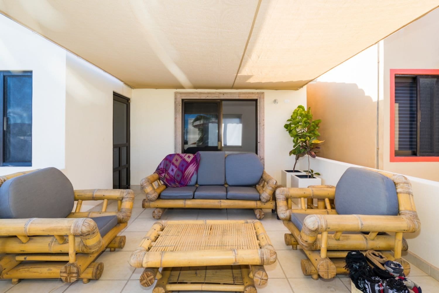Shaded outdoor terrace lounge at Outsite Los Cabos with bamboo furniture set and palm tree views