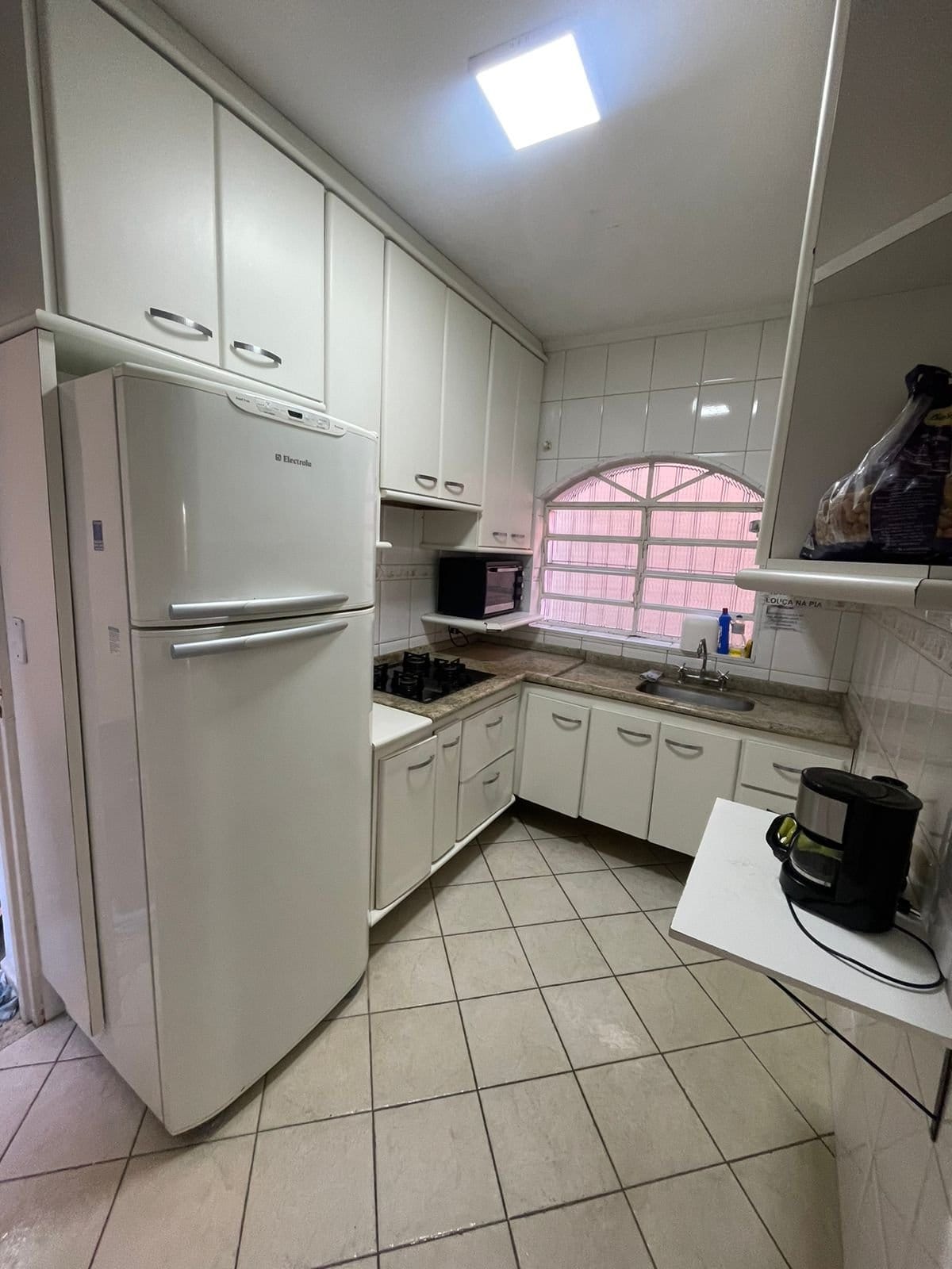Equipped shared kitchen with fridge, stove and arched window at Coliving Brooklin in São Paulo