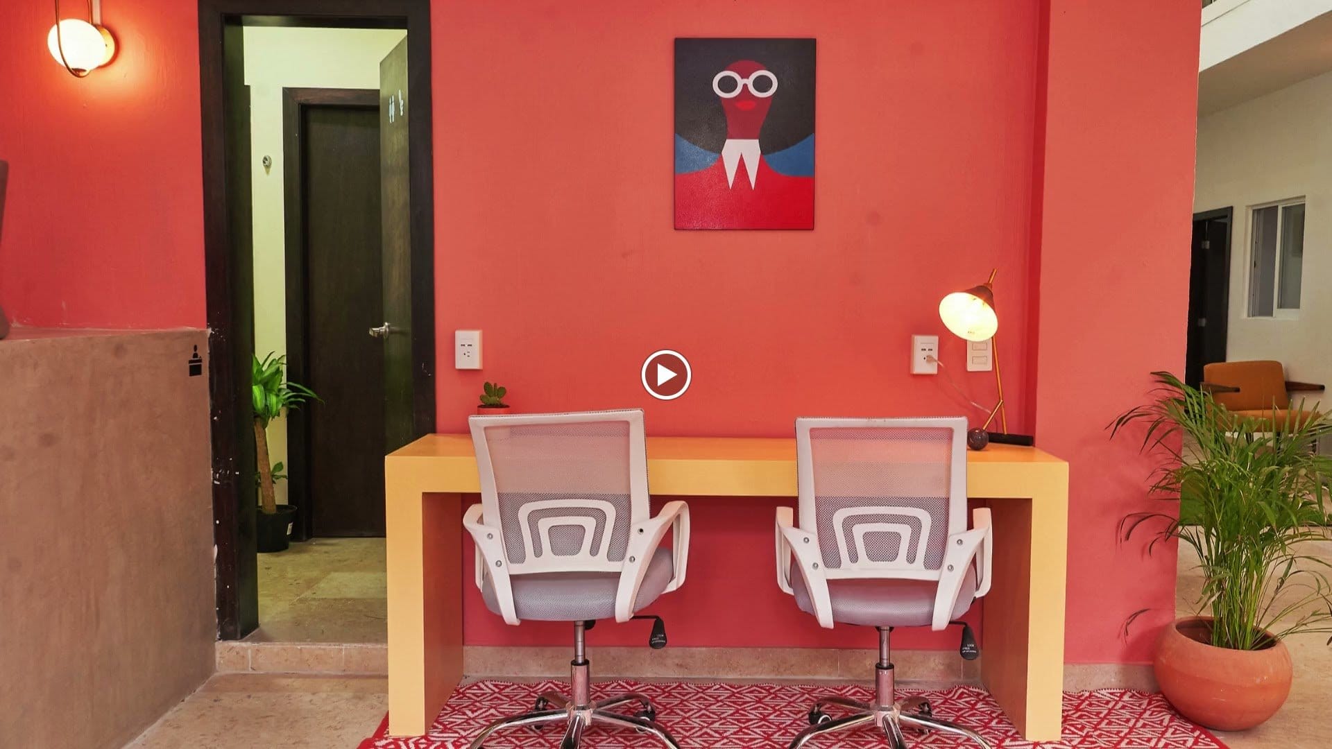 Dedicated workspace at Nora Coliving Guadalajara — two ergonomic mesh chairs at the red-walled desk area