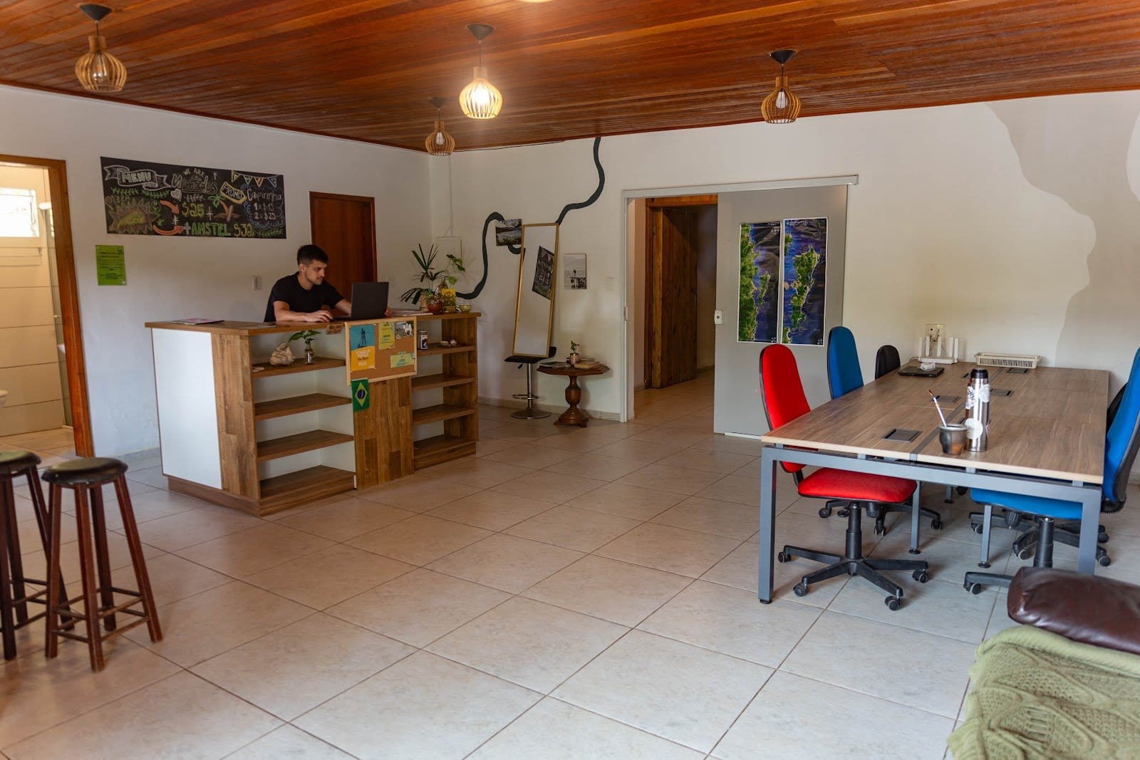 Coworking and reception area with a guest working on a laptop and a shared desk at Nômades Riverside, Florianópolis