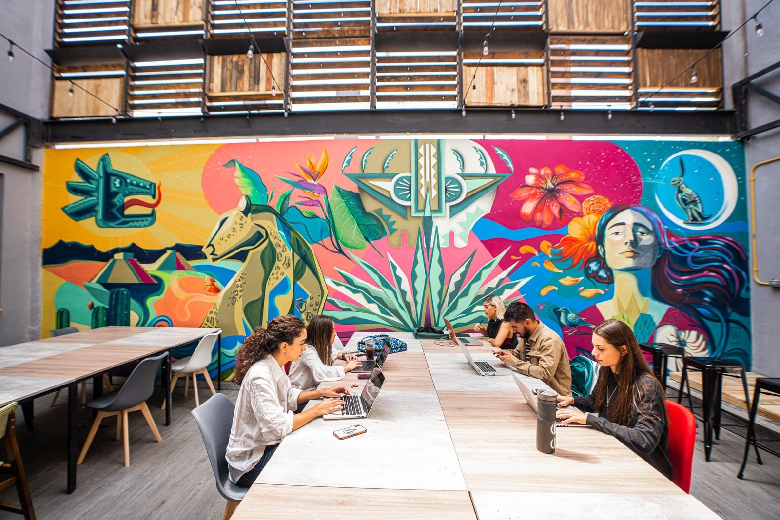 Residents working at laptops in the main coworking space at U-Co Roma in front of the vibrant Mexican mural
