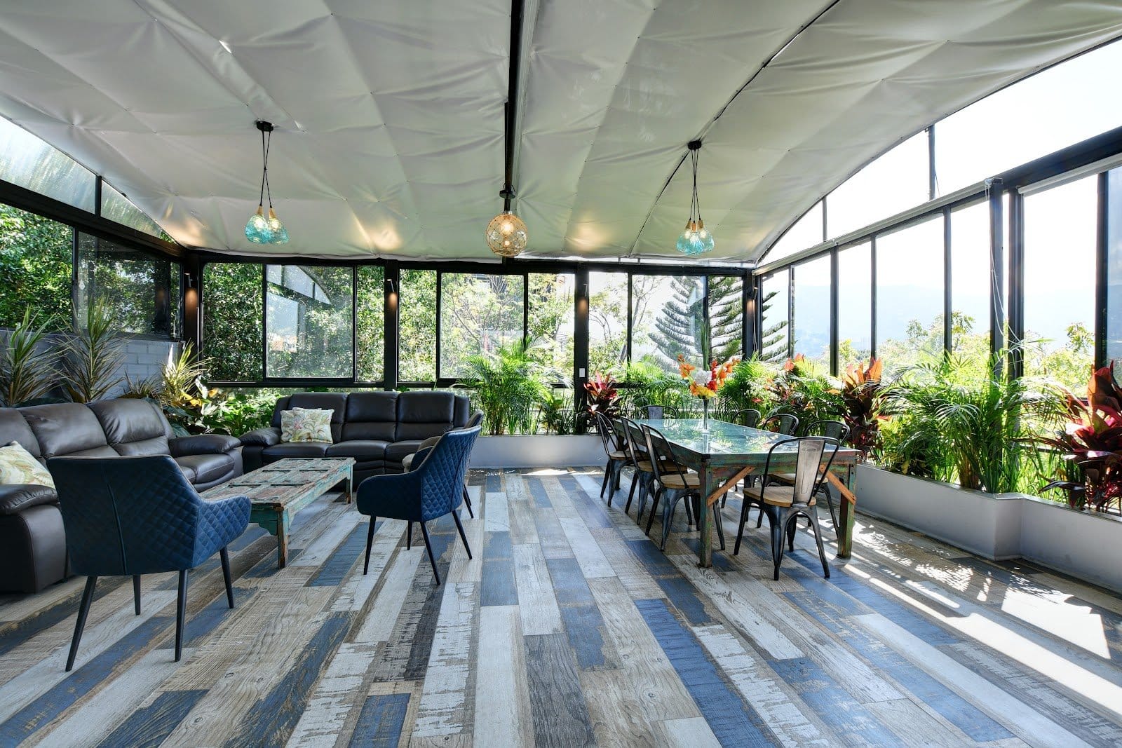 International House Co-Living glass-walled sunroom lounge and dining area filled with plants overlooking the Medellin valley