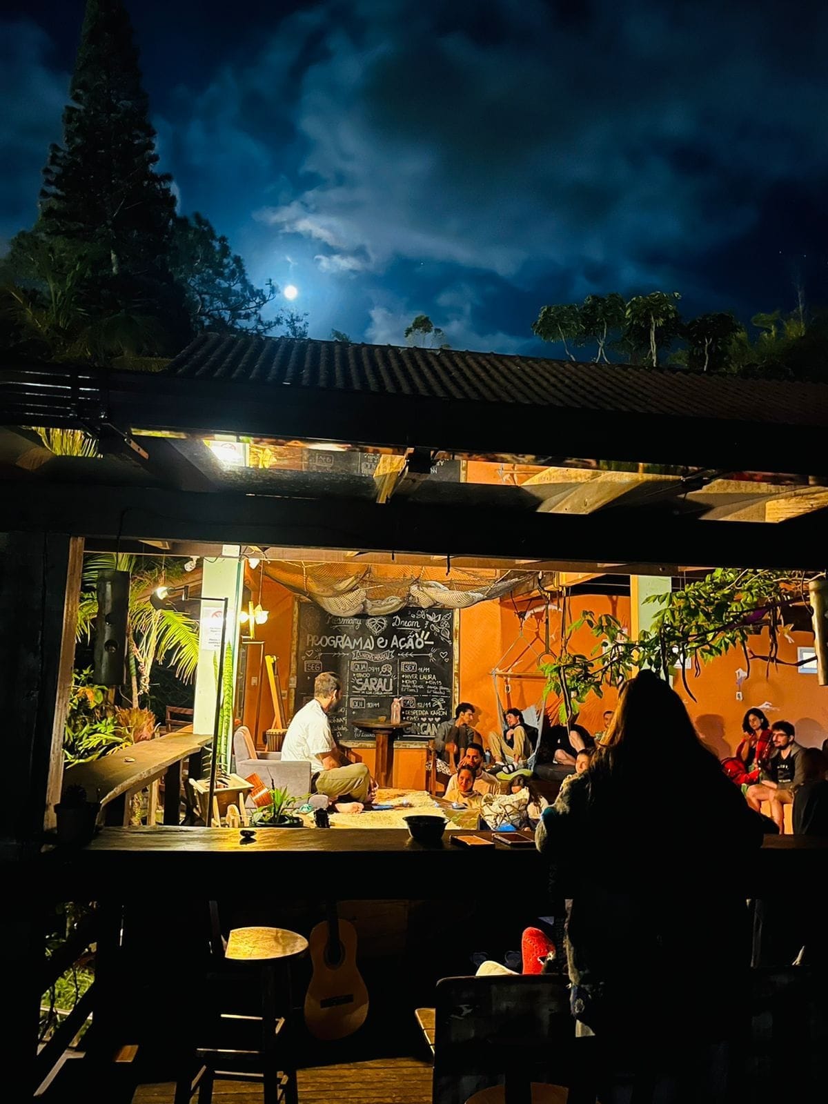 Guests socializing in the open-air common space under a full moon at Rosemary Dream Hostel & Coliving, Florianópolis
