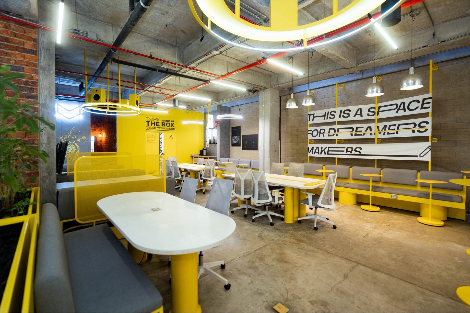The Box coworking room at Indie Studio with yellow desks, ergonomic chairs and a 'space for dreamers and makers' mural in Medellín