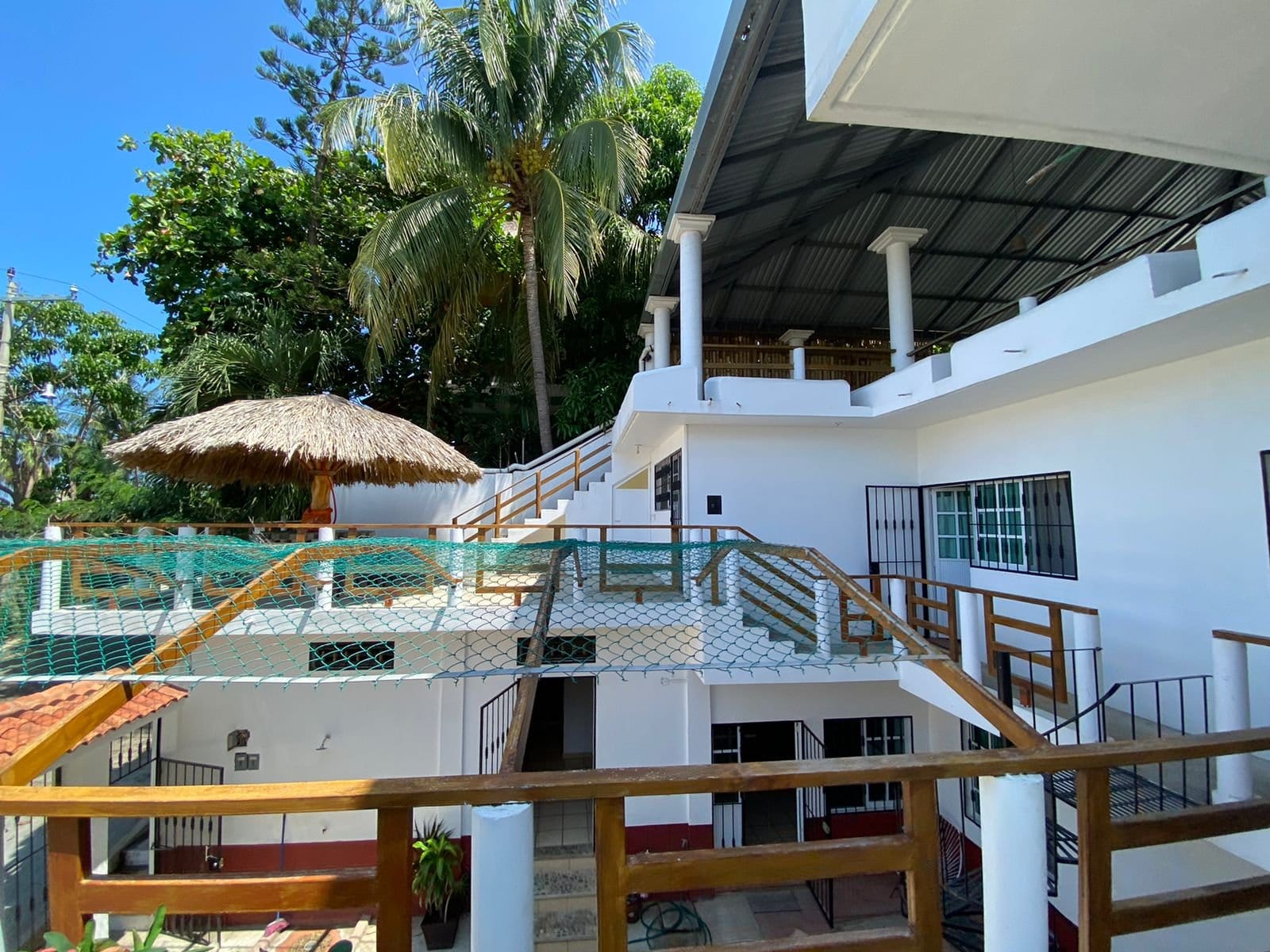 Multi-level exterior of Flow Coliving Puerto Escondido showing palapa terrace, hammock net and upper floors