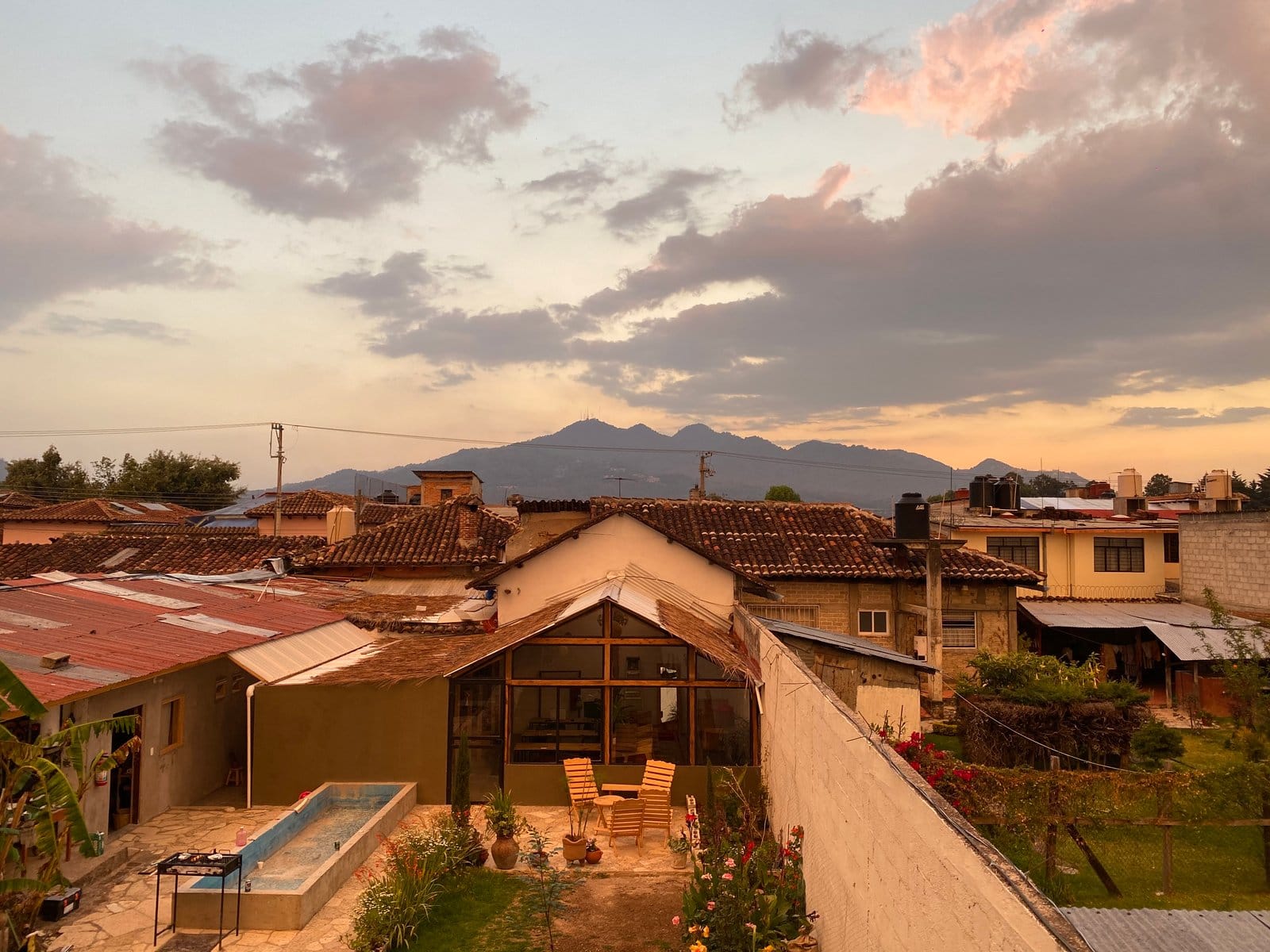 Aerial view of Co404 San Cristóbal courtyard — greenhouse coworking, plunge pool, and mountain backdrop at golden hour