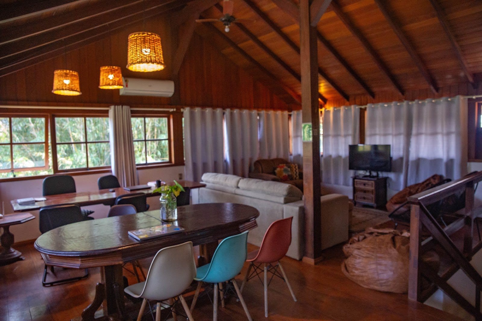 Warm wood-ceilinged common lounge with a dining table, sofa and beanbags at Nômades Riverside, Florianópolis