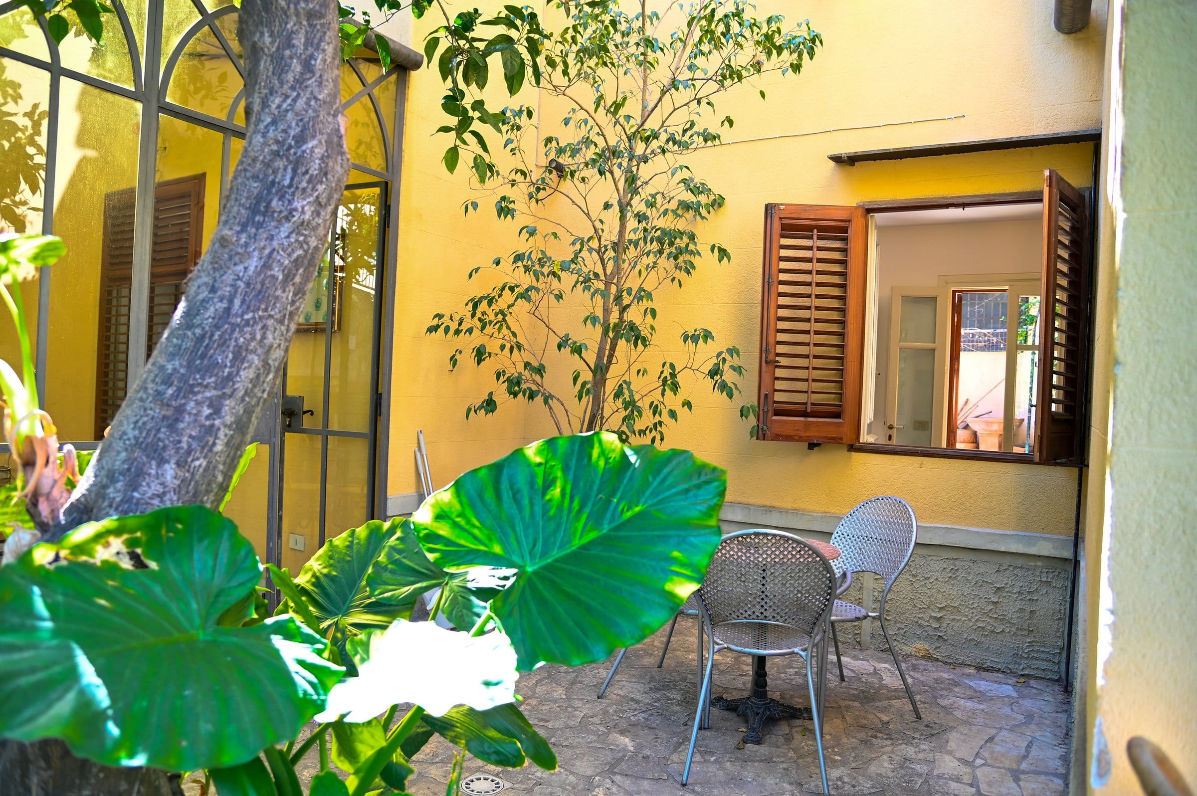 BeetCommunity garden courtyard with bistro seating against the yellow facade amid lush tropical foliage