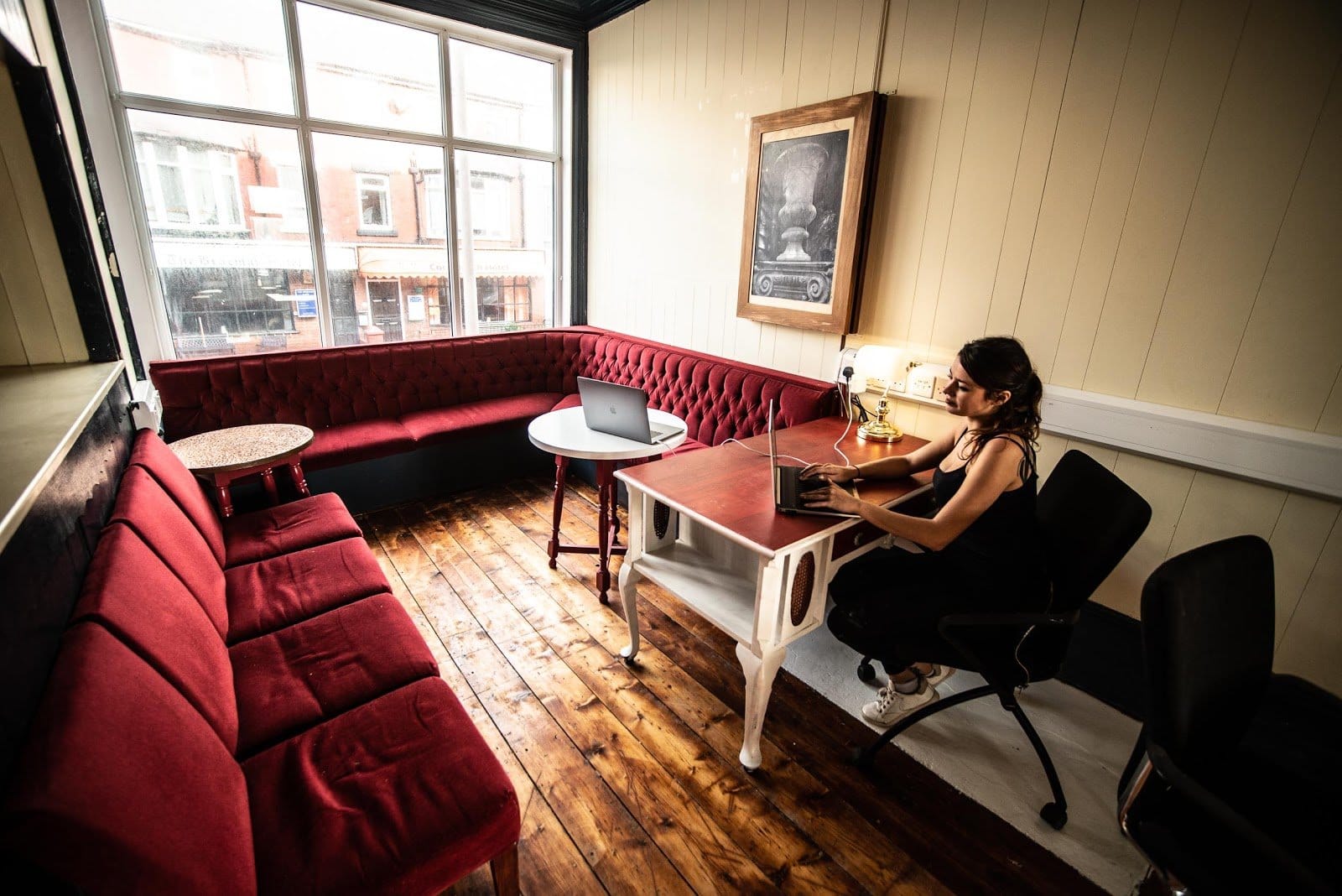Cozy coworking space with a burgundy couch, two tables, and a person working on a laptop.