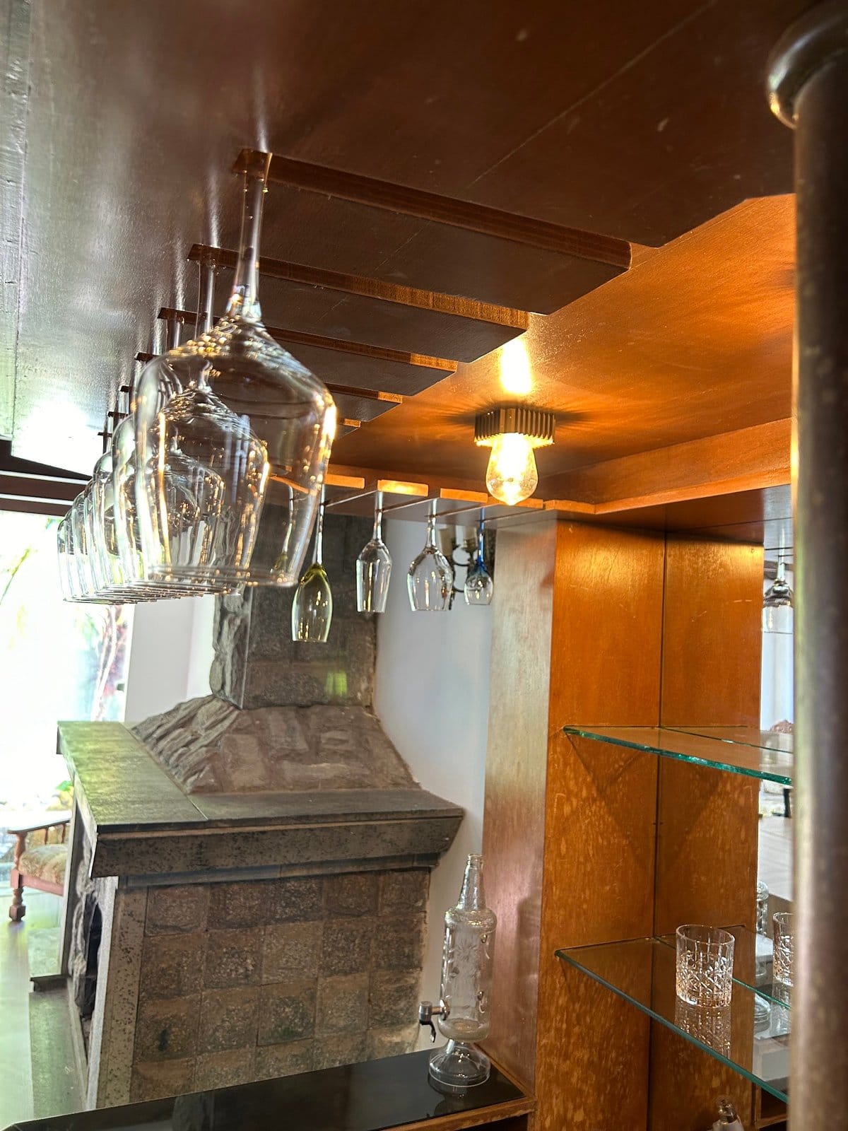 Cozy bar nook with hanging glassware and a stone fireplace at Horizonte Coliving