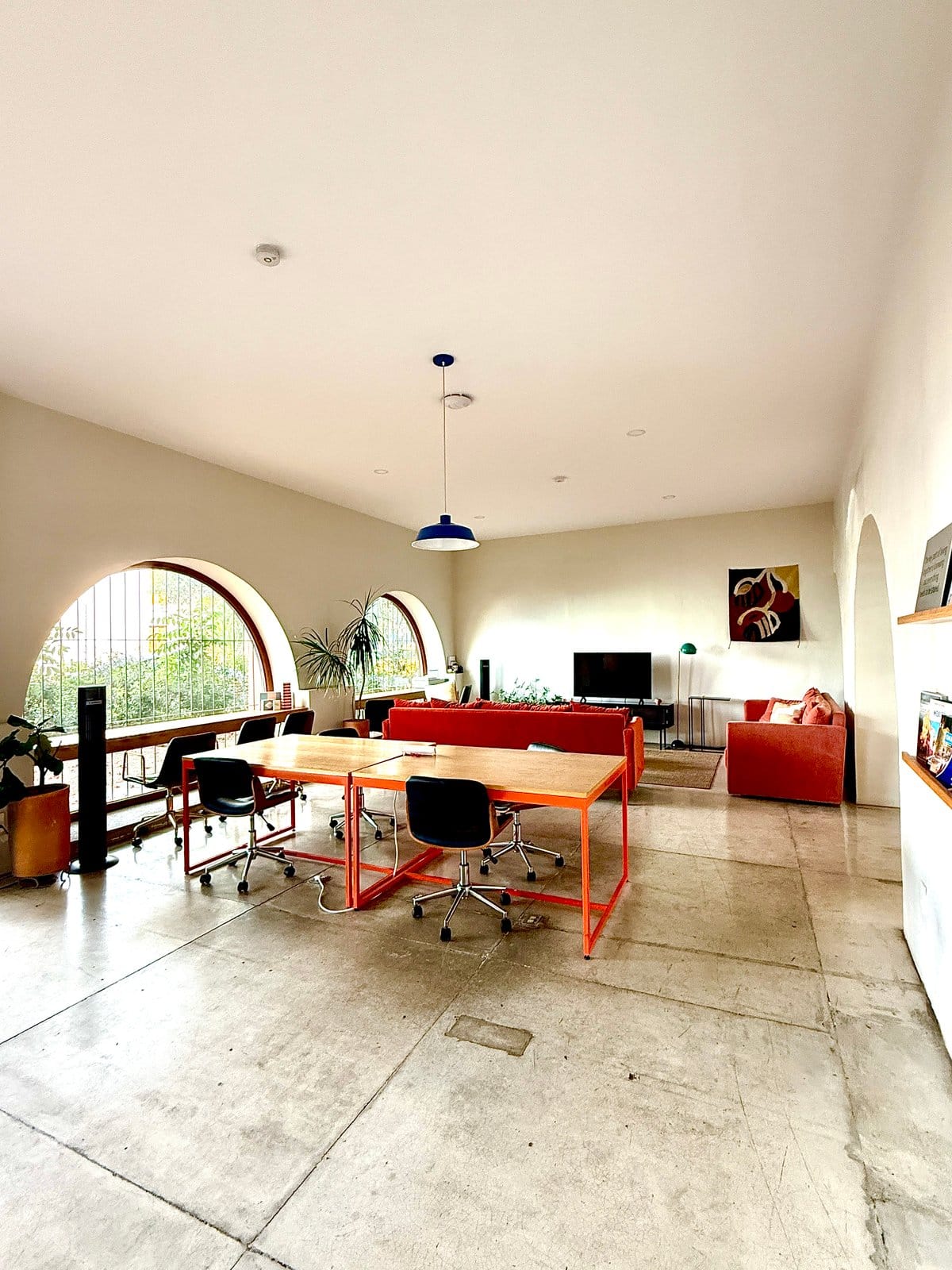Coworking space at Outsite Oaxaca City — orange-framed desks and task chairs beneath arched windows overlooking the garden
