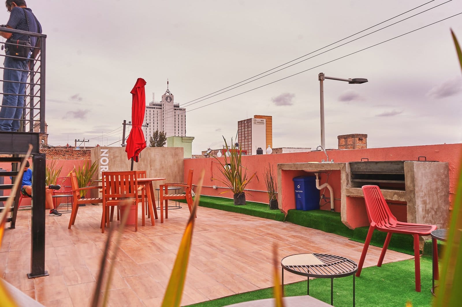 Nora Coliving rooftop terrace with red chairs and barbecue area, city skyline of Guadalajara visible