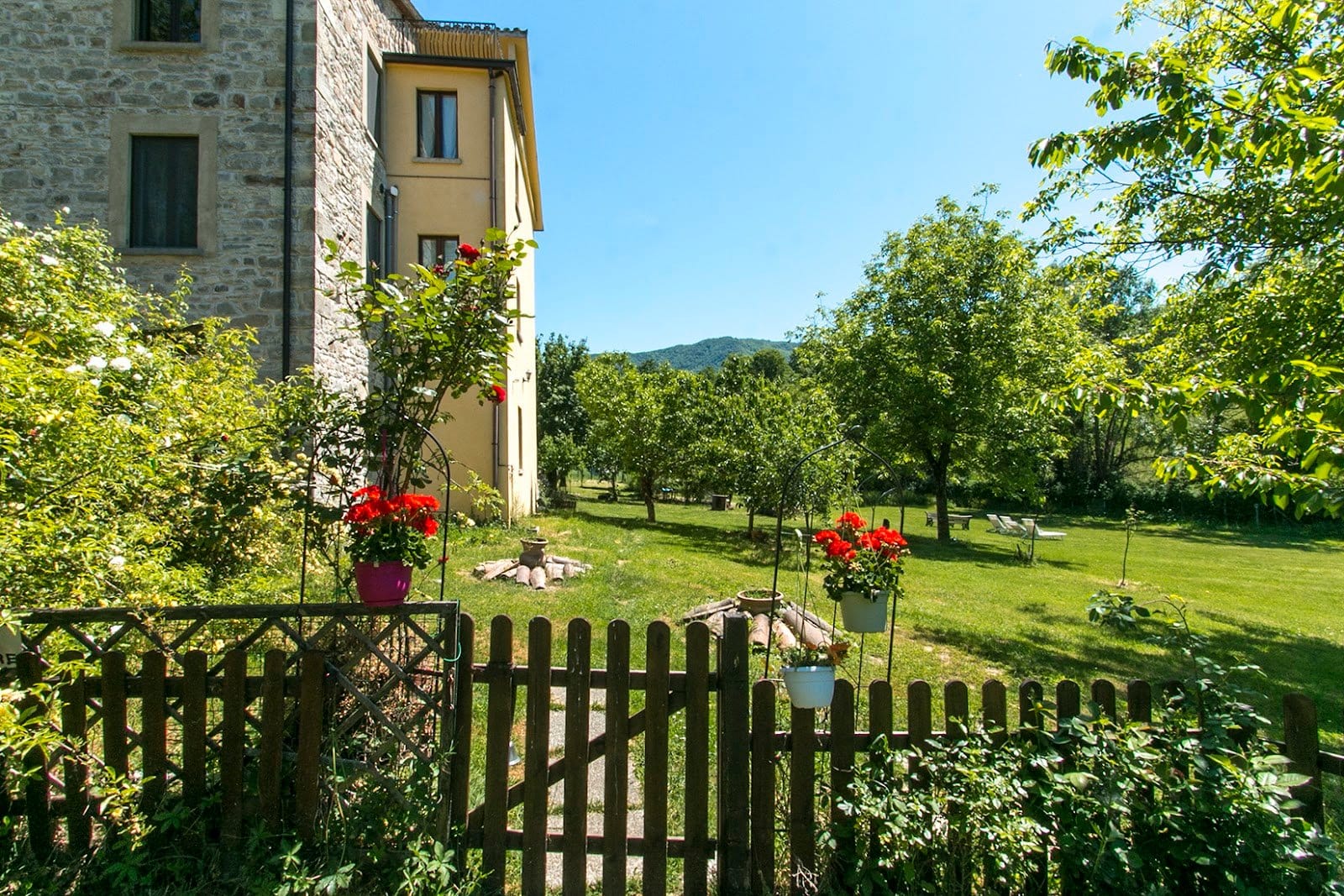 Garden scene with flowers and lawn area beside a light yellow stone building under sunlight.