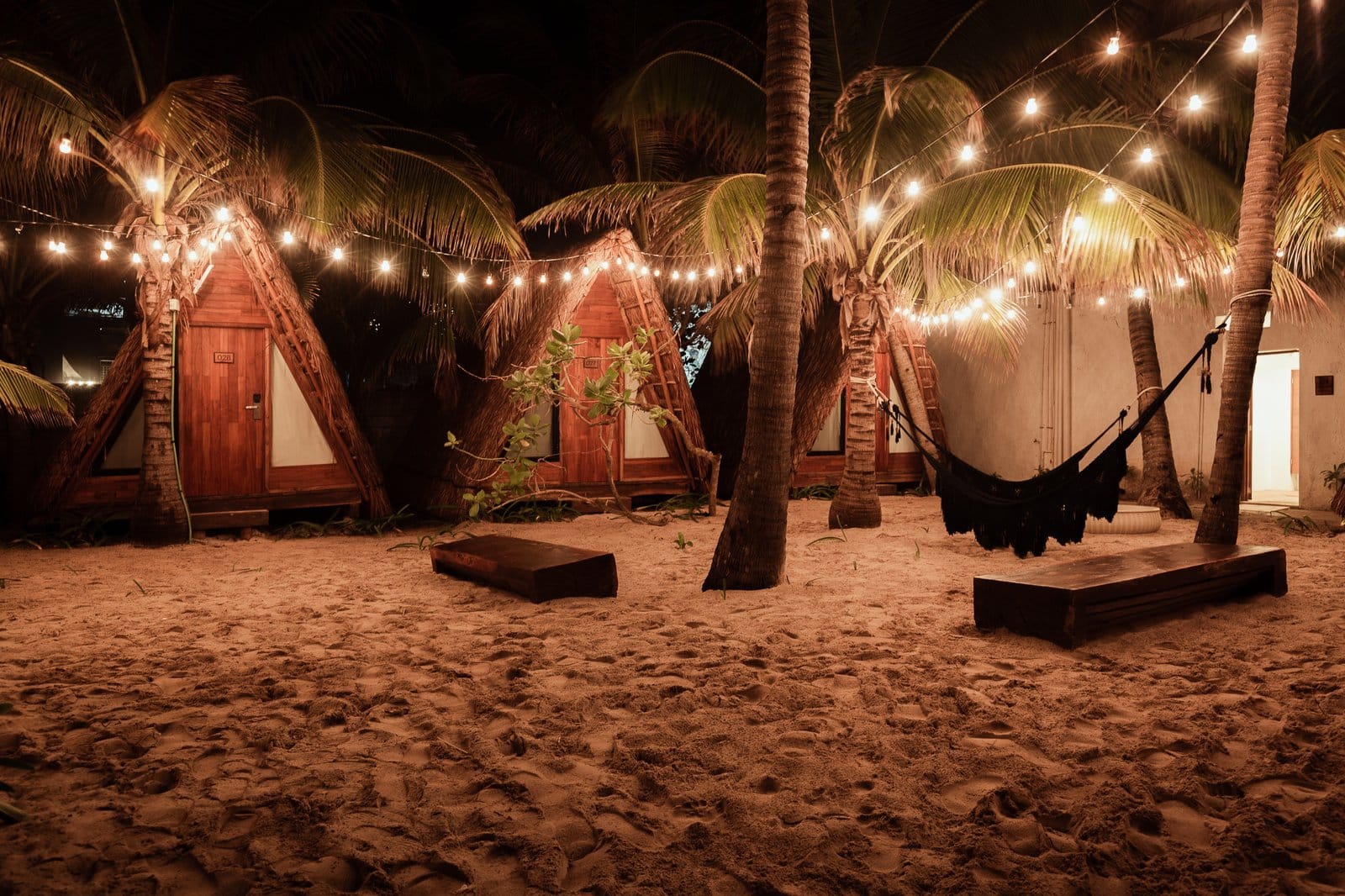 A-frame bungalows at Selina Isla Mujeres lit by warm string lights at night with a hammock and white sand beach