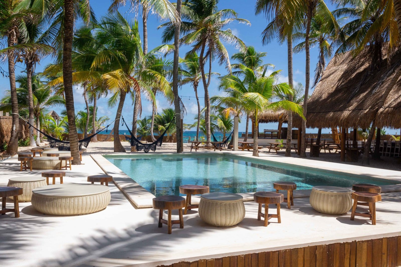 Pool at Selina Isla Mujeres with wicker lounge chairs, hammocks between palm trees and the Caribbean sea in the background