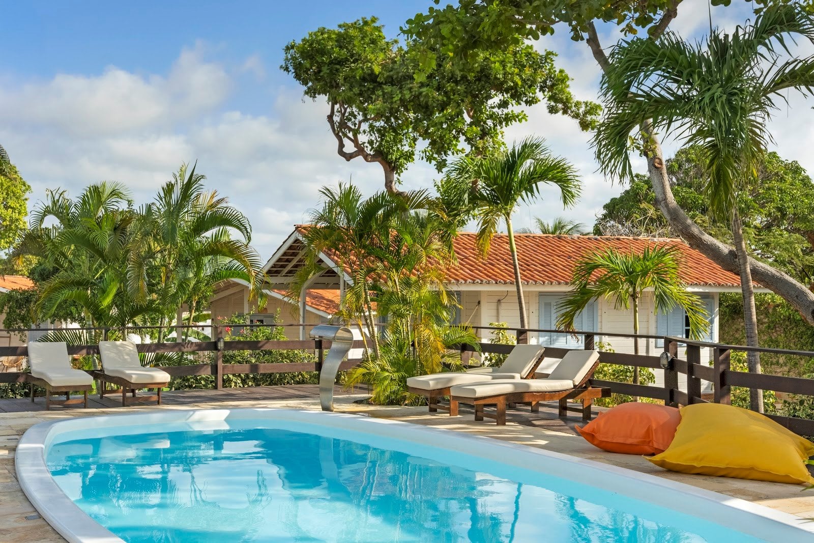 Pool with loungers and bean bags framed by palm trees and bungalows at FlowHouse Jeri