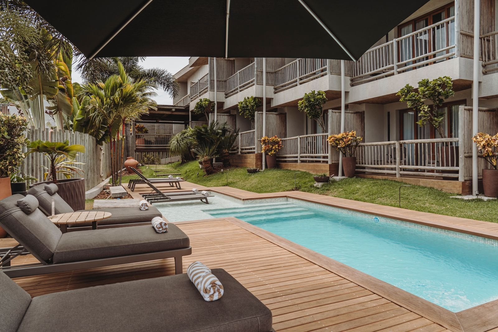 Poolside loungers under a parasol beside the pool and balconied guest building at Pousada Maria Bonita, Fernando de Noronha