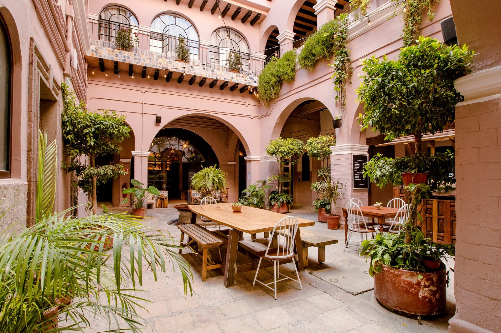 Lush colonial courtyard at Selina San Miguel de Allende with long communal table, tropical plants, and arched balconies on two floors