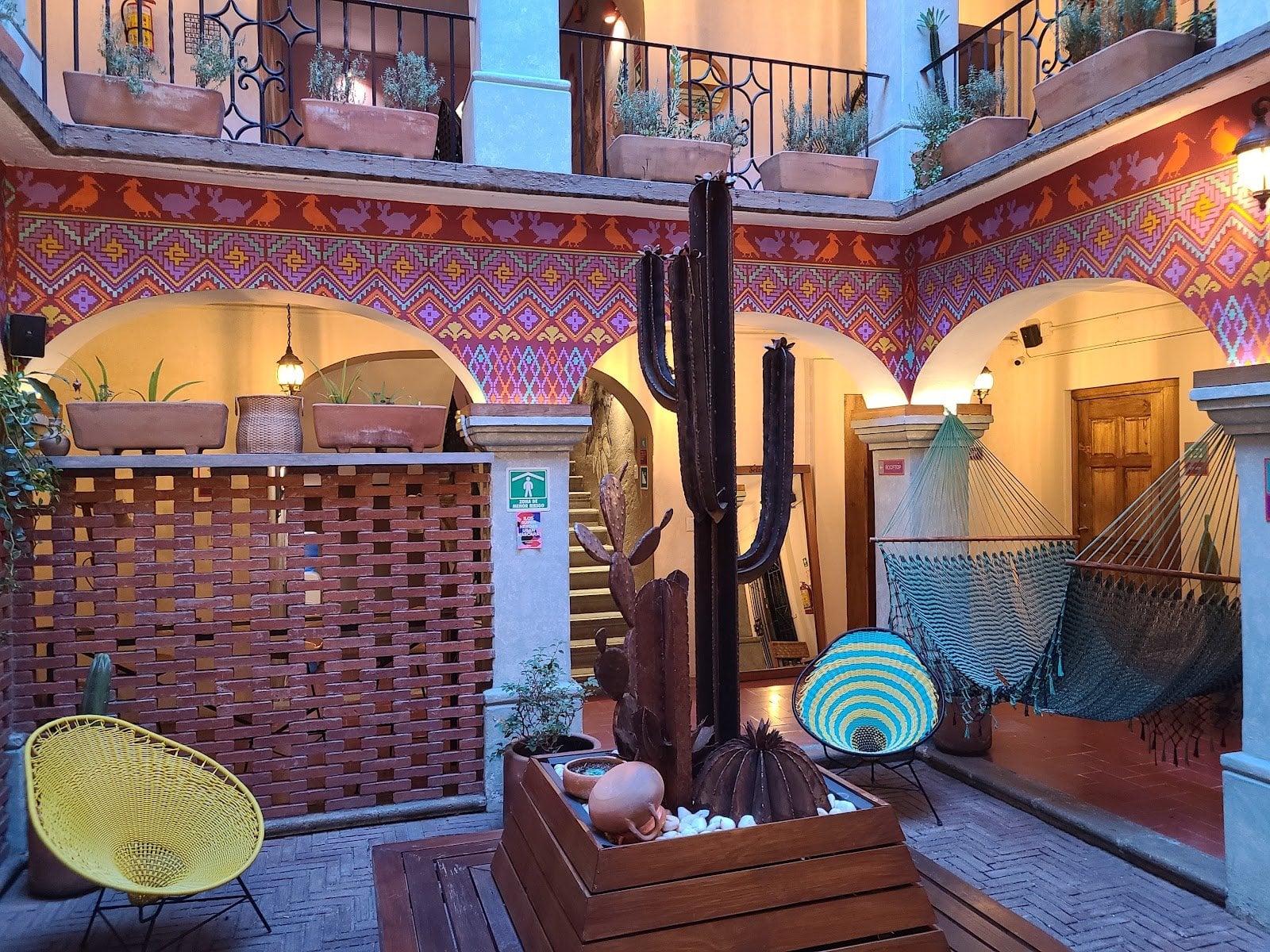 The colonial courtyard at Selina Oaxaca glowing in warm evening light, with a yellow Acapulco chair and hanging hammock framed by terracotta geometric latticework, arched balconies and a towering cactus