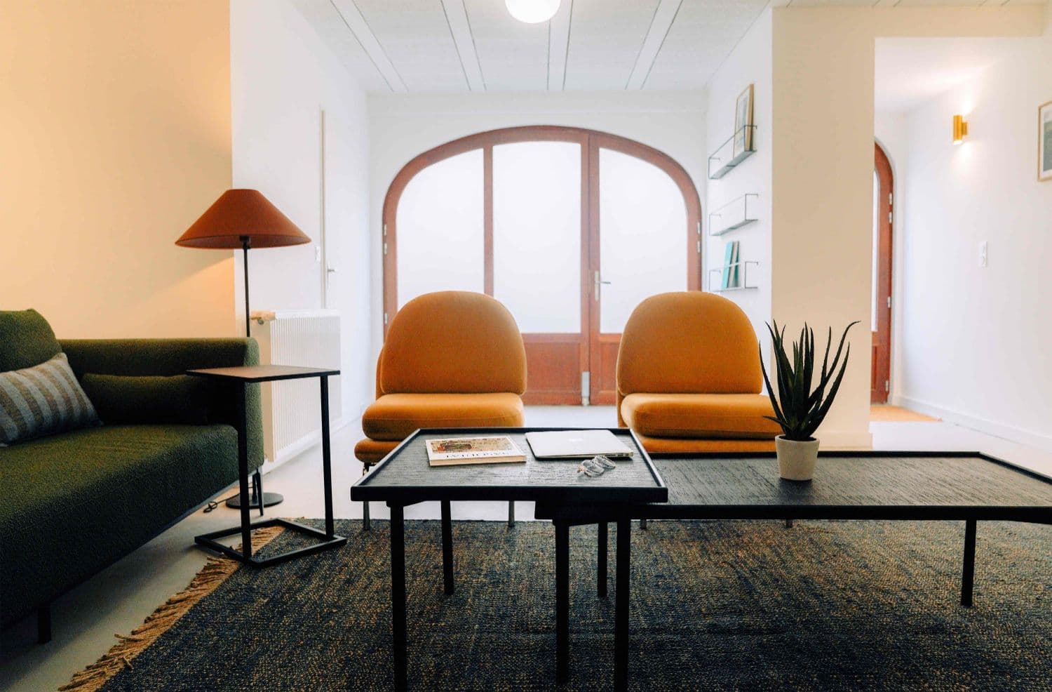 Wide lounge at Outsite Bordeaux with green sofa, mustard chairs, arched window doors, and soft natural light