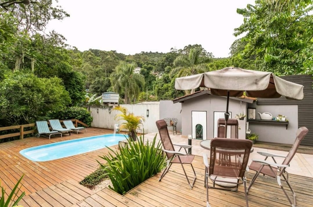 Poolside deck with loungers, umbrella and dining set overlooking the green hillside at Coliving Casa Jerivá in Florianópolis
