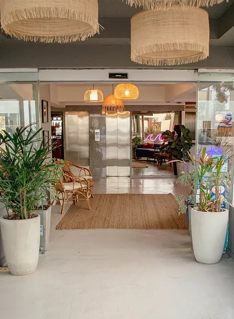 Open, warmly lit lobby or common area with plants, wicker chairs, and pendant lights