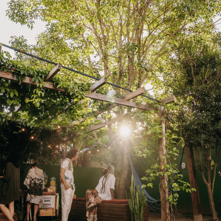 Lush garden courtyard with string lights and golden-hour sunlight, a few residents relaxing at Coliving Muní in Florianópolis