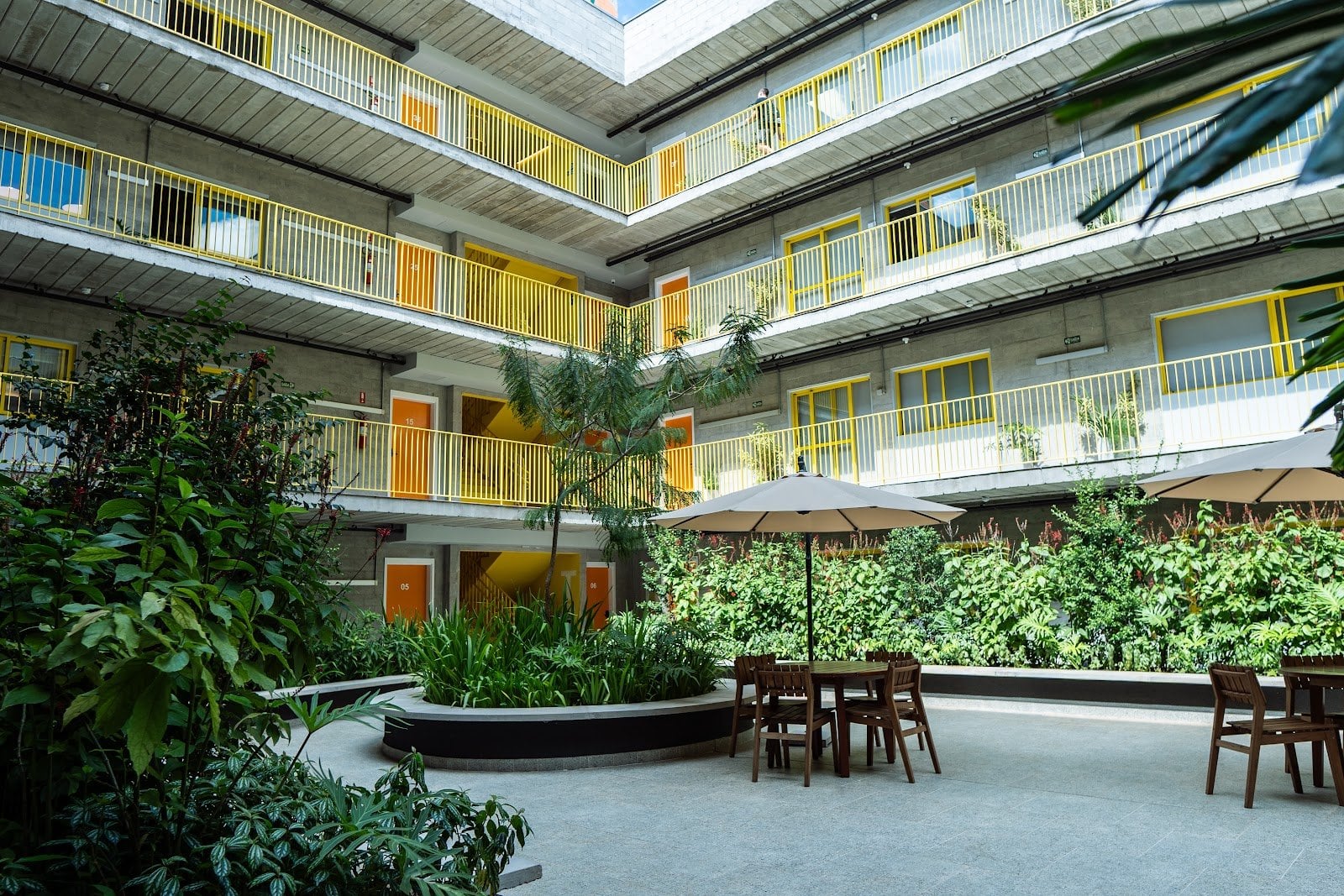 Landscaped interior courtyard with umbrellas and yellow balconies at Uliving Campinas