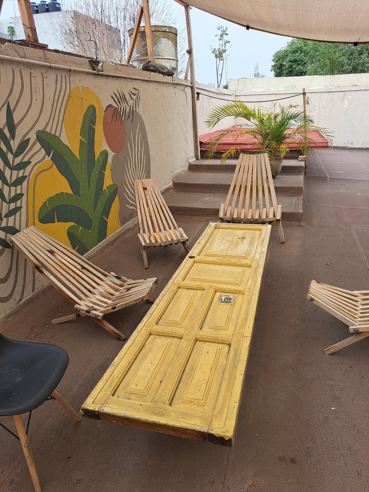 Rooftop terrace at Co404 Oaxaca with botanical mural, wooden lounge chairs, and upcycled door table
