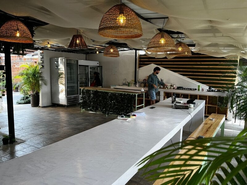 Open-air communal kitchen and bar with woven pendant lights and plants at Co404 Medellin