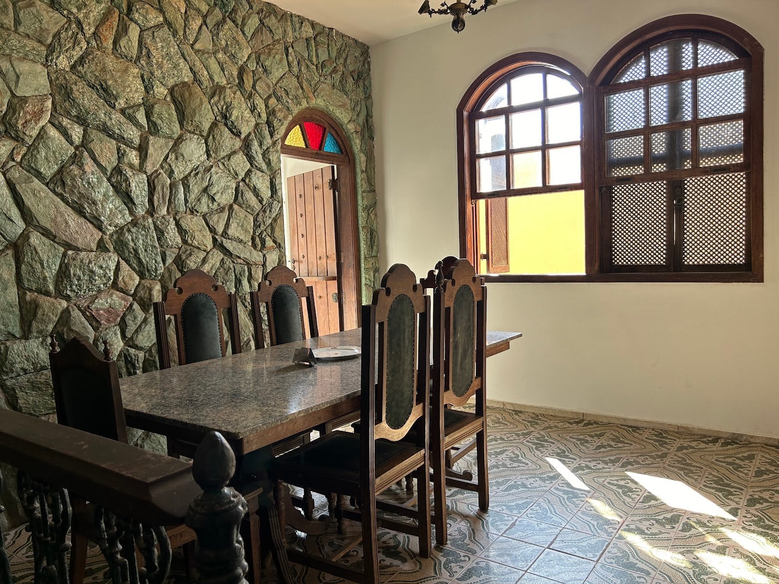 Communal dining room with stone wall, stained-glass window and long wooden table at Horizonte Coliving